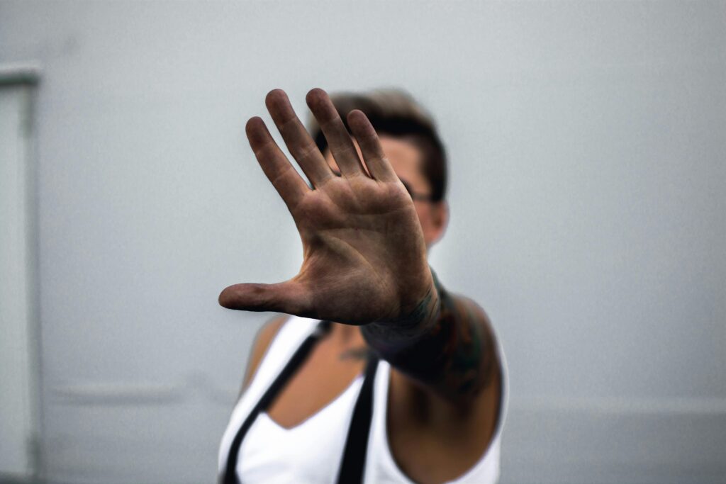 Close-up of a person's hand raised in a stop gesture, against a neutral background.