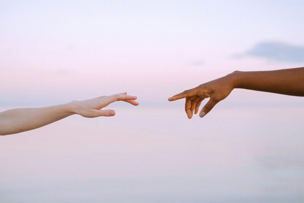 Two diverse hands reaching out across a pastel horizon, symbolizing unity and connection.