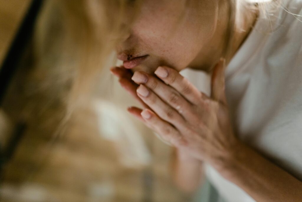 A close-up of a woman's face showing a bruise and hands touching her lips, indoors.