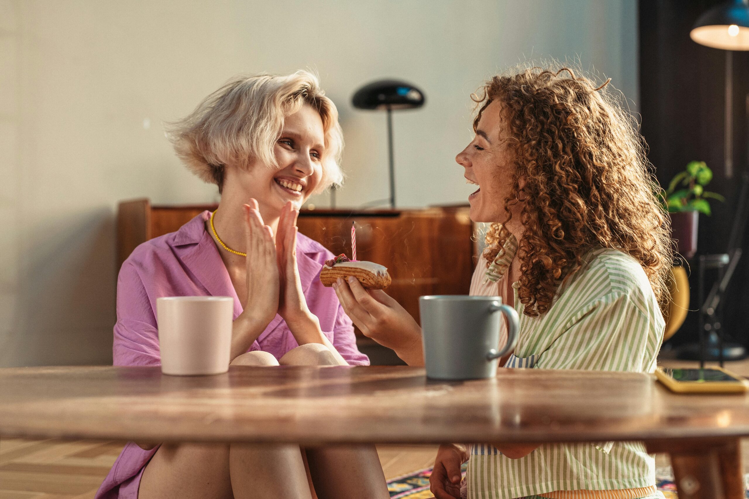 Two friends sharing a joyful moment indoors with coffee and a cake.